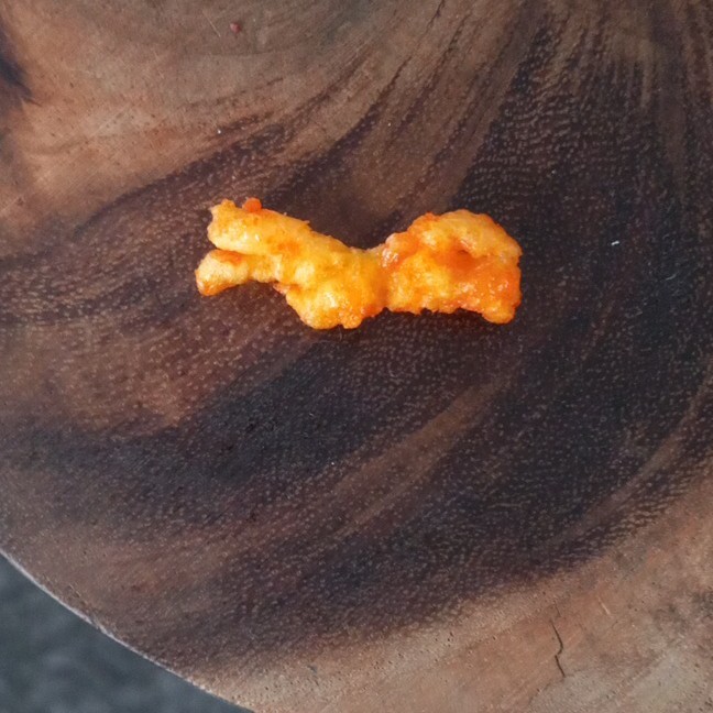 Single Orange Puffed Snack Piece (Cheeto-Style) on Wooden Surface